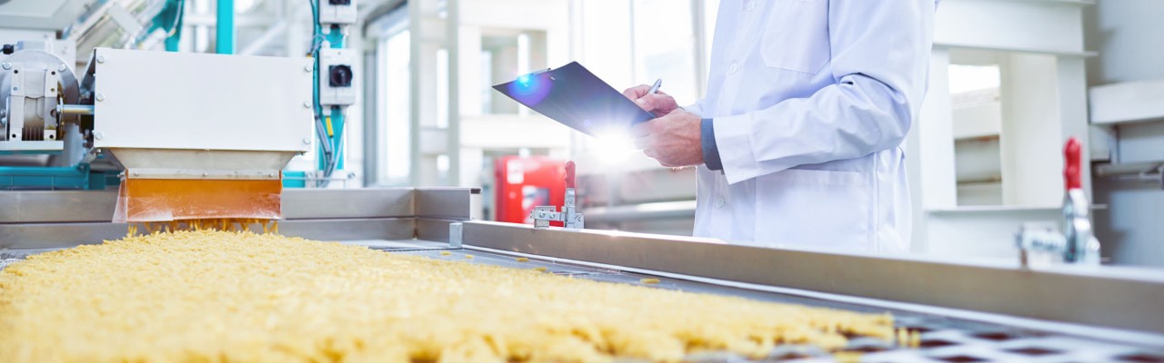 Side view portrait of senior factory worker  in food industry holding clipboard standing by conveyor belt, copy space