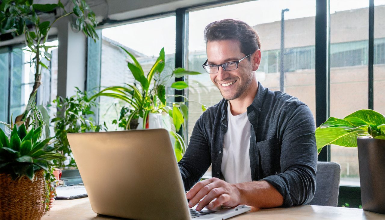 man smiling at laptop screen in a bright office